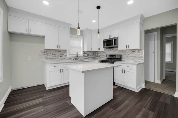 a kitchen with stainless steel appliances granite countertop a sink a microwave oven a refrigerator and white cabinets with wooden floor