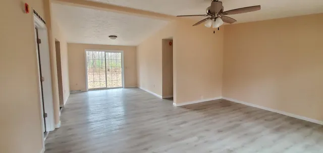 an empty room with wooden floor fan and windows