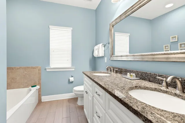 a bathroom with a granite countertop double vanity sink a mirror and a bathtub