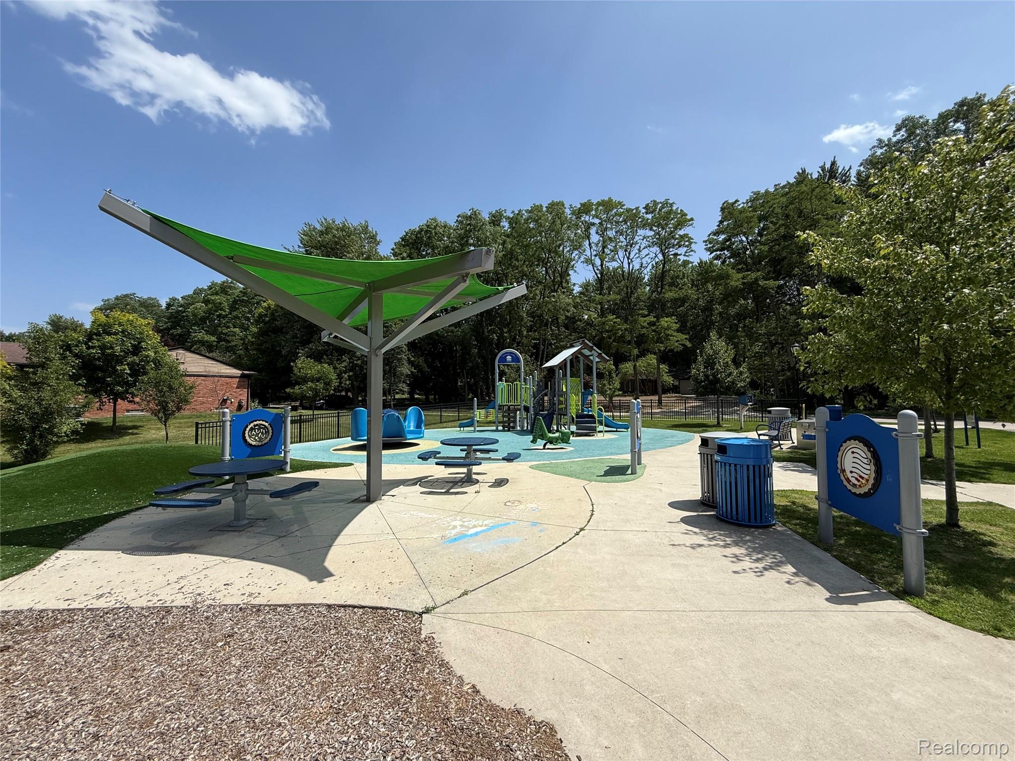 39909 Lynn Street Canton, MI 48187 - Photo 44 of 45 Community playground featuring a shade structure, multiple play areas, picnic tables, and concrete pathways, all surrounded by mature trees