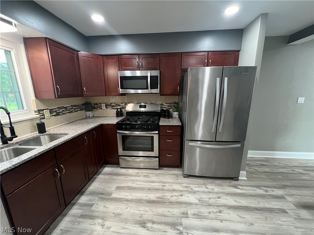 7475 Selwick Drive Parma, OH 44129 - Photo 9 of 29 Kitchen featuring light stone countertops, light hardwood / wood-style flooring, stainless steel appliances, backsplash, and sink