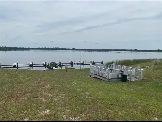 a view of a lake with lawn chairs and large trees