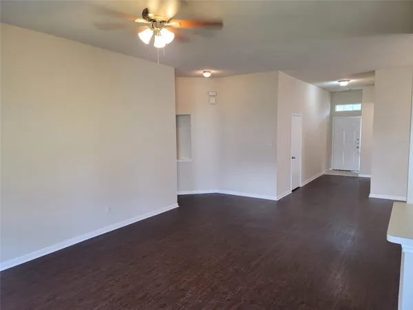 a view of an empty room with wooden floor and a ceiling fan