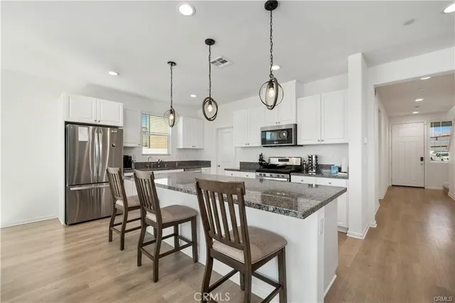 a kitchen with stainless steel appliances granite countertop a stove a sink a refrigerator a dining table and chairs with wooden floor