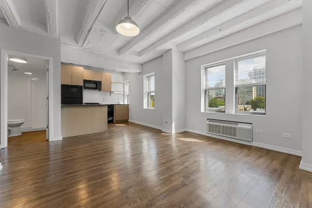 an empty room with wooden floor and a kitchen