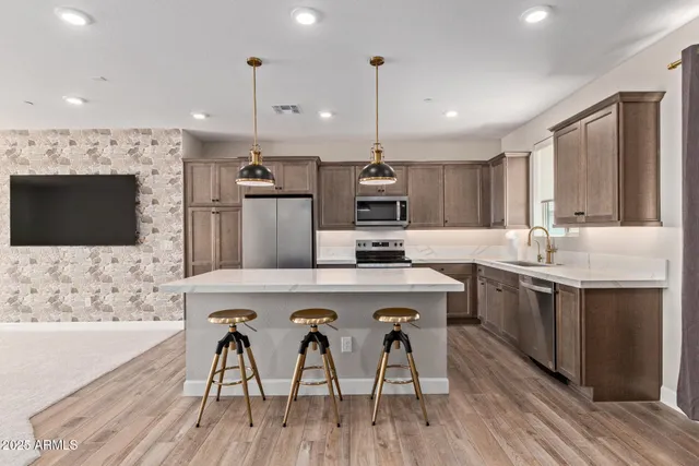 a kitchen with stainless steel appliances a stove a sink a microwave a refrigerator and white cabinets with wooden floor