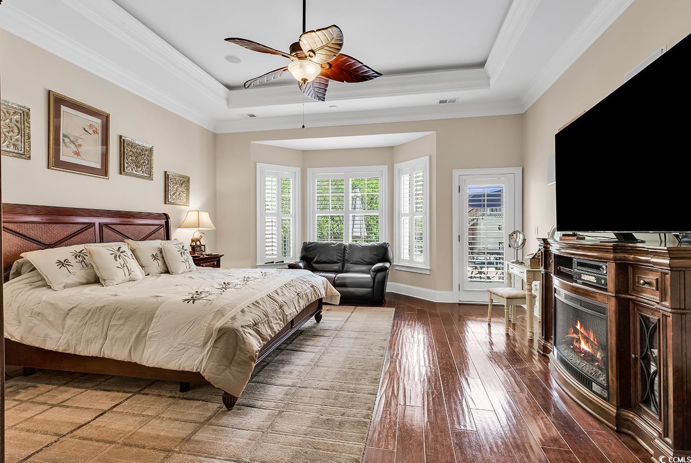 487 Trestle Way Conway, SC 29526 - Photo 15 of 40 Bedroom featuring a tray ceiling, a warm lit fireplace, wood-type flooring, access to outside, and crown molding