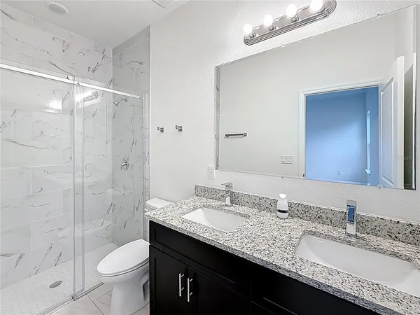 a bathroom with a granite countertop sink a toilet a shower and a mirror