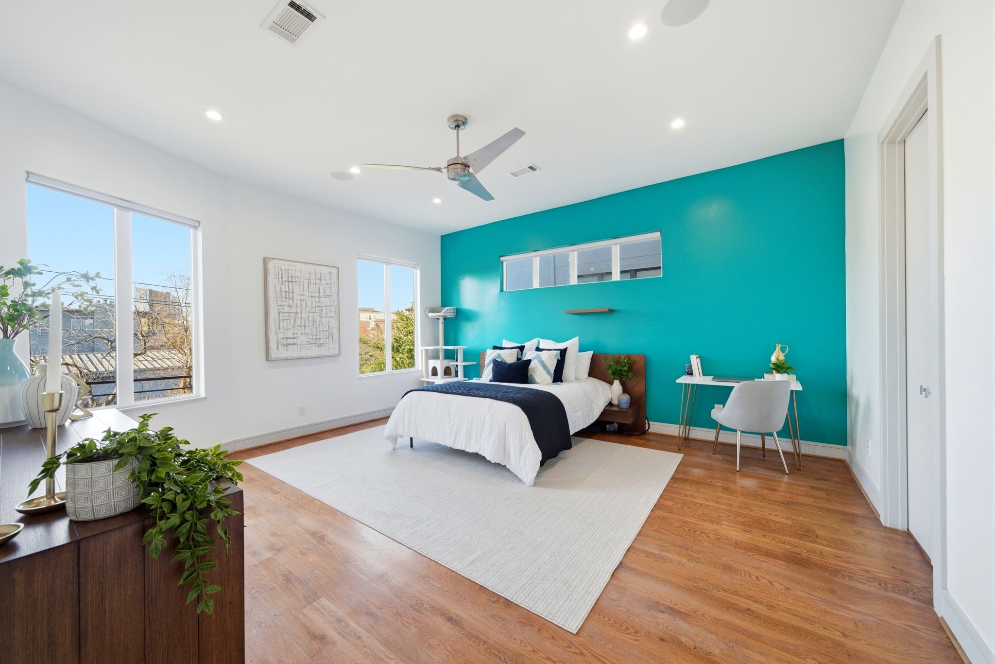 1405 Vermont Street, Unit A Houston, TX 77006 - Photo 27 of 46 Bold teal feature accent wall creates a striking contemporary focal point in this expansive primary bedroom. Polished hardwoods and high ceilings enhance the spacious layout, which comfortably accommodates a king-size bed and a dedicated workspace. Large windows flood the room with natural light, offering a bright and airy retreat at 1405 Vermont Street #A.