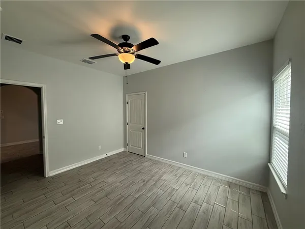 an empty room with wooden floor fan and windows