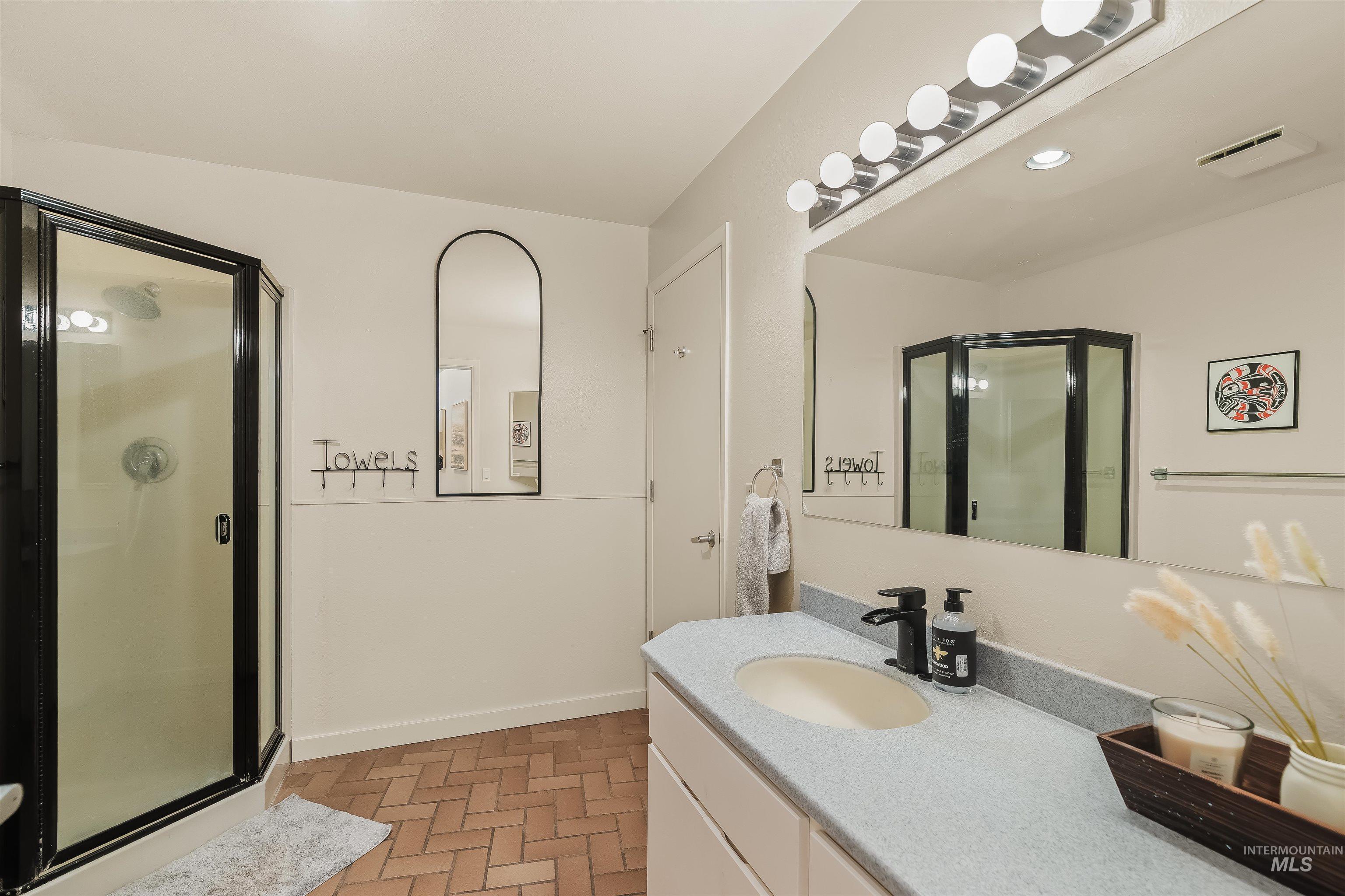 2048 Arborcrest Road Moscow, ID 83843 - Photo 28 of 50 Corner shower with black trim, vanity with integrated sink, large wall-mounted mirror, modern light fixture, and brick-patterned flooring