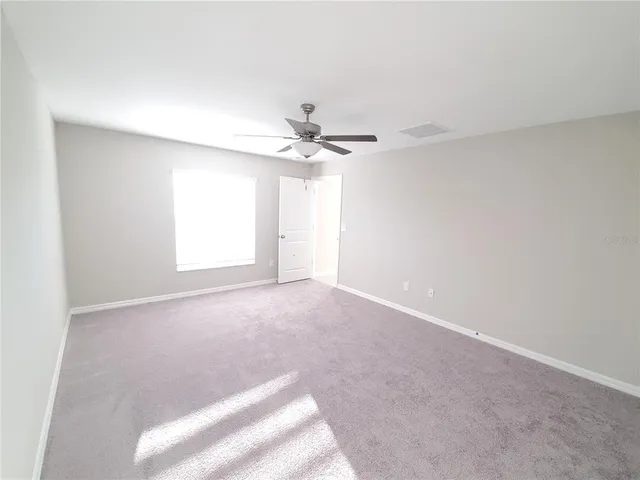 an empty room with chandelier fan and windows