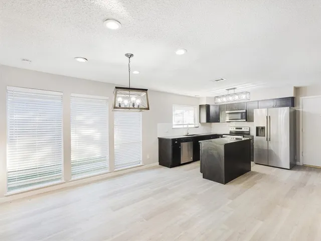 a large kitchen with a large counter top a refrigerator and cabinets