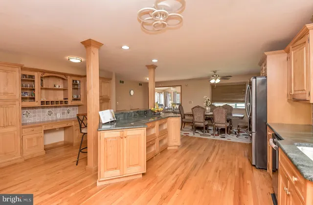 a kitchen with stainless steel appliances granite countertop a stove top oven a refrigerator a dining table and chairs with wooden floor