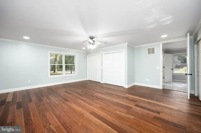 an empty room with wooden floor ceiling fan and window