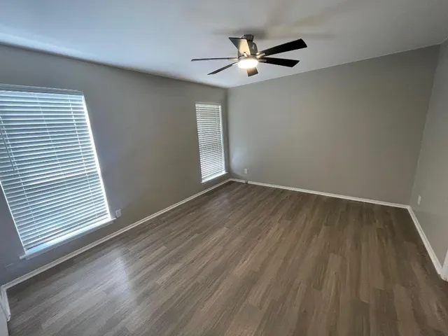 an empty room with wooden floor fan and windows