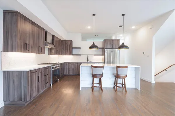 a kitchen with stainless steel appliances granite countertop a stove a sink a refrigerator a dining table and chairs with wooden floor