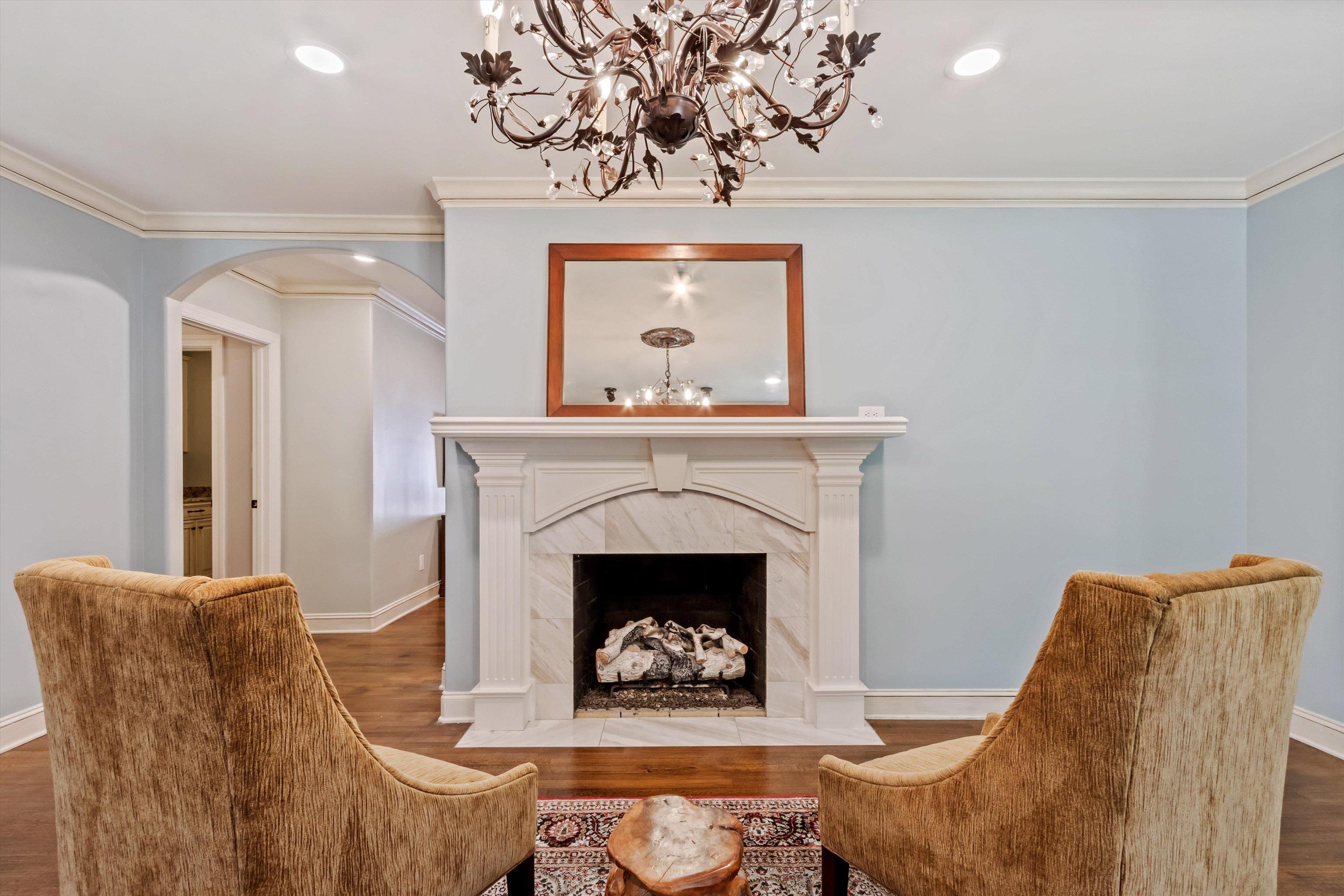 5302 South Angela Road Memphis, TN 38120 - Photo 10 of 40 Living area featuring a white stone fireplace with an ornate mantel, hardwood-style flooring, a decorative chandelier, recessed ceiling lighting, and crown molding