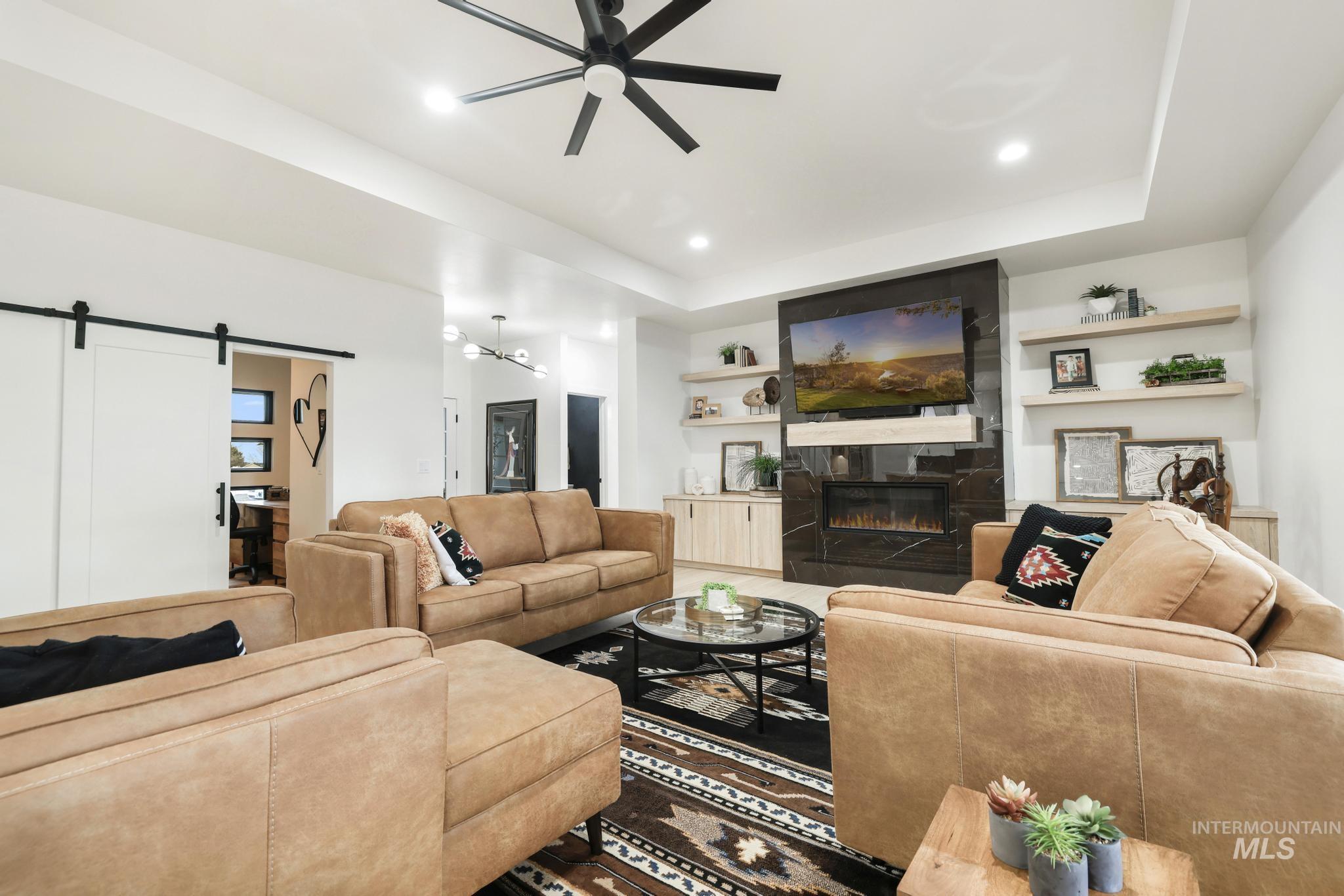 3140 Moonrise Road Twin Falls, ID 83301 - Photo 5 of 39 Living area featuring a barn door, ceiling fan, a raised ceiling, a glass covered fireplace, and recessed lighting
