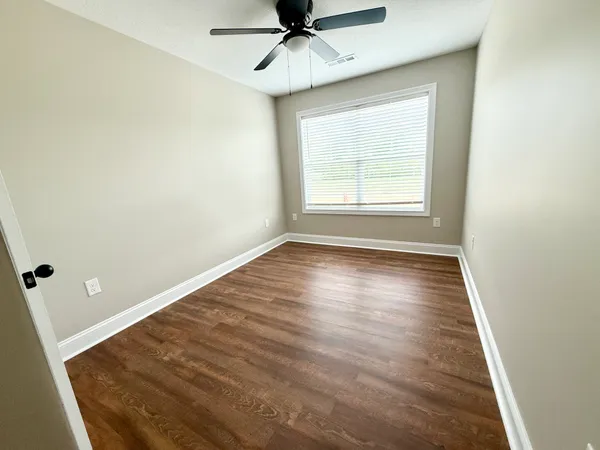 an empty room with wooden floor fan and windows