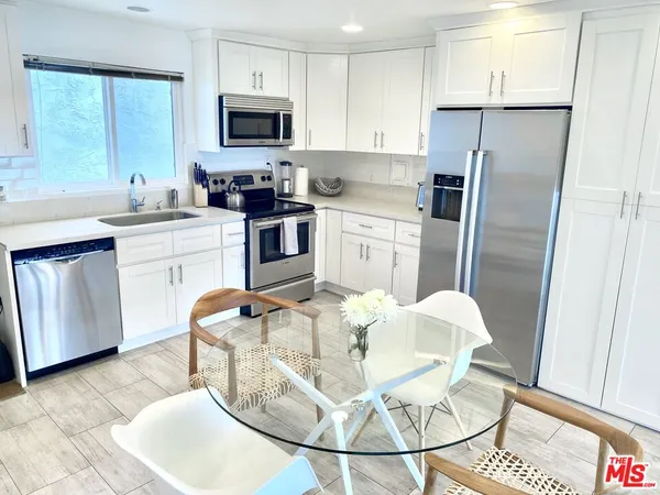 a kitchen with stainless steel appliances a dining table a microwave a refrigerator and cabinets