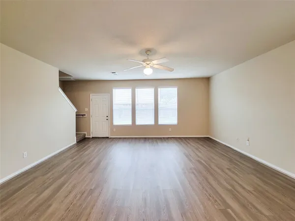 an empty room with wooden floor chandelier fan and windows