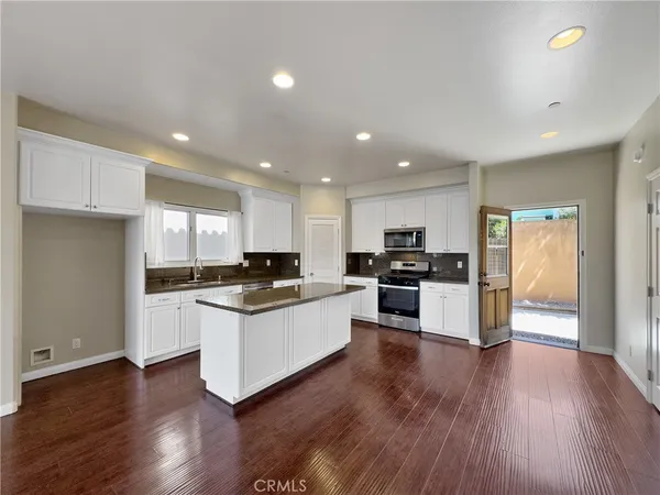 a kitchen with stainless steel appliances kitchen island granite countertop a stove top oven a sink a refrigerator and white cabinets with wooden floor