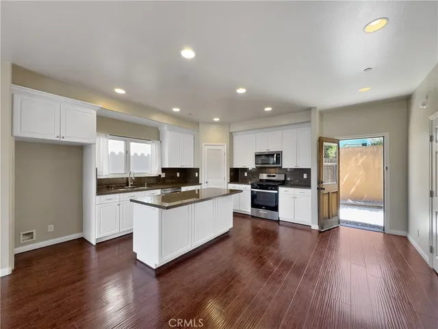 a kitchen with stainless steel appliances kitchen island granite countertop a stove top oven a sink a refrigerator and white cabinets with wooden floor