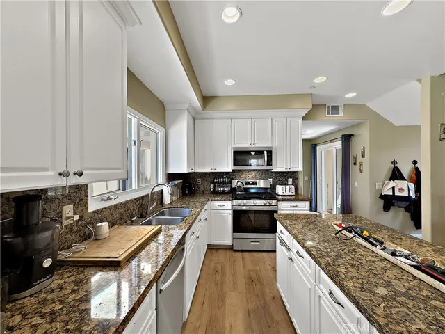 a kitchen with stainless steel appliances granite countertop a stove top oven a sink dishwasher and a refrigerator with wooden floor