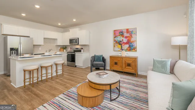 a living room with stainless steel appliances furniture a rug and a kitchen view