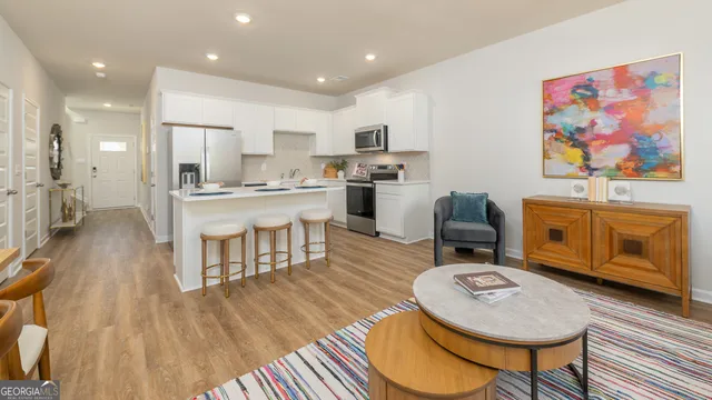 a living room with stainless steel appliances furniture a rug and a kitchen view