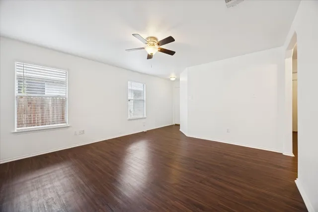 a view of an empty room with wooden floor and a ceiling fan