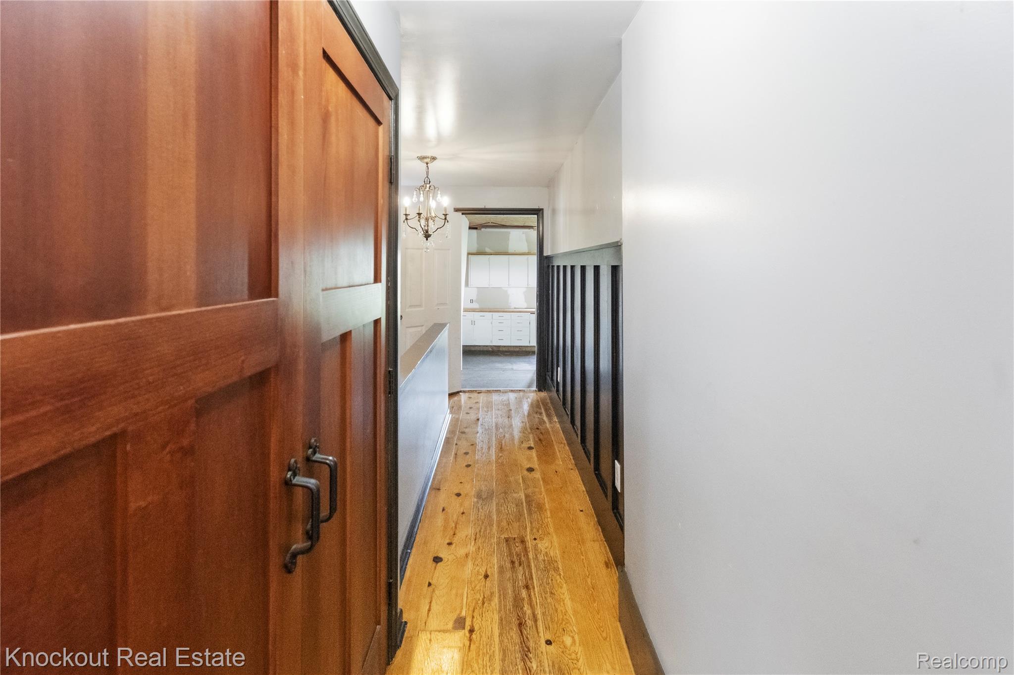 5750 Maple Road Frankenmuth, MI 48734 - Photo 32 of 60 Wood-finish flooring, paneled wood door with dark hardware, dark accent wainscoting, and a decorative chandelier