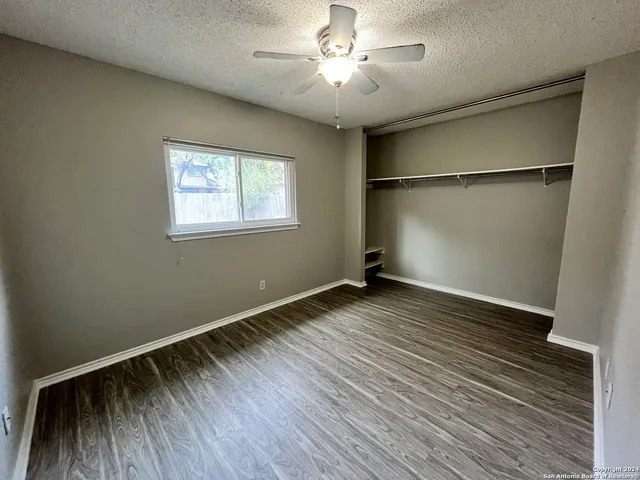 an empty room with wooden floor chandelier fan and windows