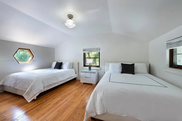a bedroom with a bed and a lamp on dresser with wooden floor