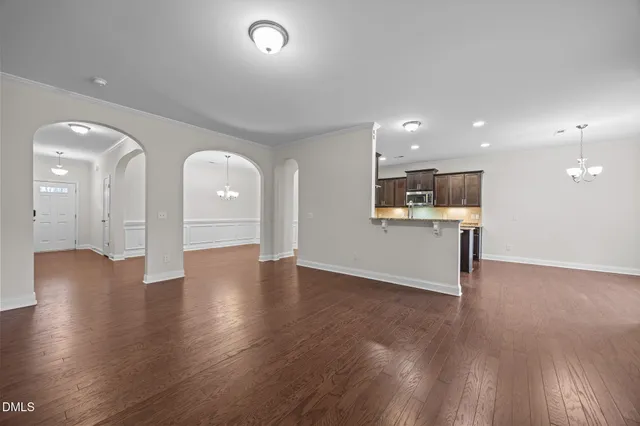 a view of an empty room with wooden floor and a kitchen