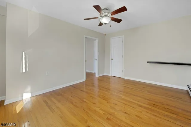a view of an empty room with wooden floor and a ceiling fan