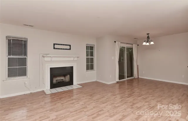 a view of an empty room with wooden floor fireplace and a window