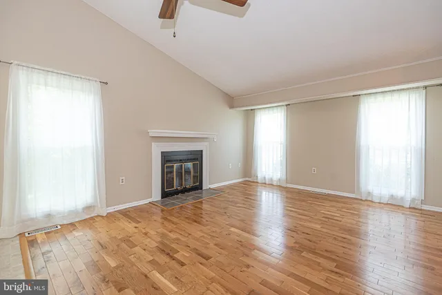 an empty room with wooden floor fireplace and windows