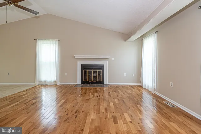 a view of an empty room with wooden floor fireplace and a window