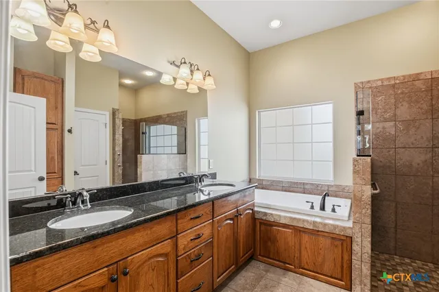 a bathroom with a granite countertop double vanity sink a mirror and a bathtub