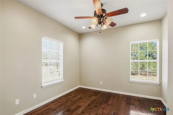 an empty room with wooden floor fan and windows