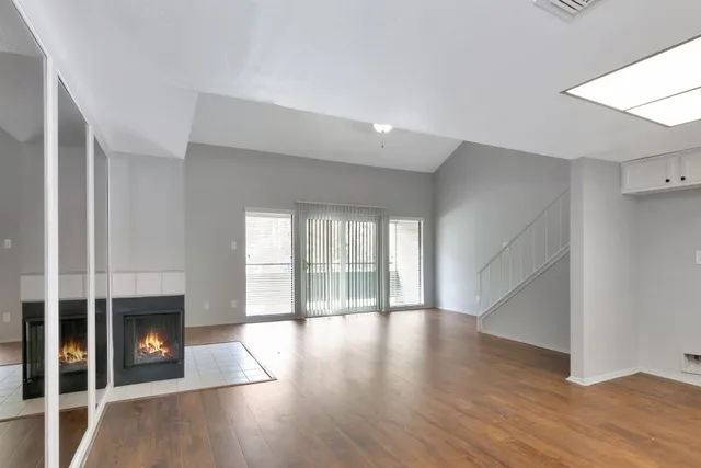 an empty room with wooden floor fireplace and windows