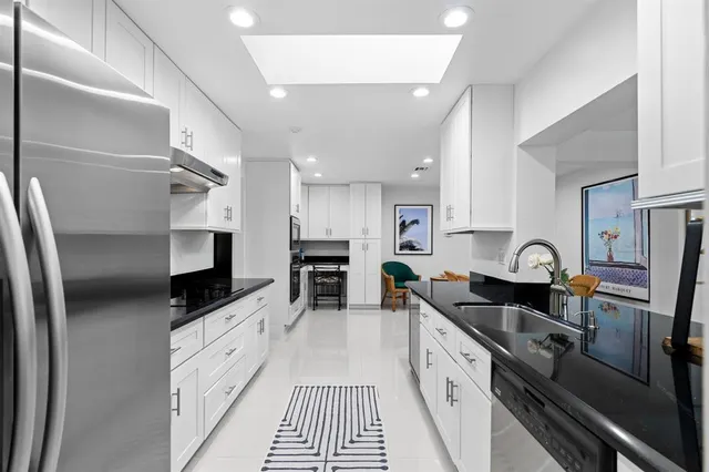 a kitchen with stainless steel appliances a sink a stove top oven a refrigerator cabinets and a dining table