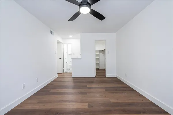 a view of an empty room with wooden floor and a ceiling fan