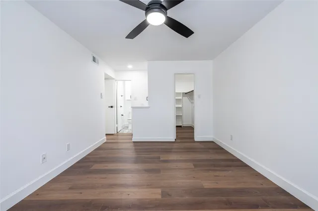 a view of an empty room with wooden floor and a ceiling fan