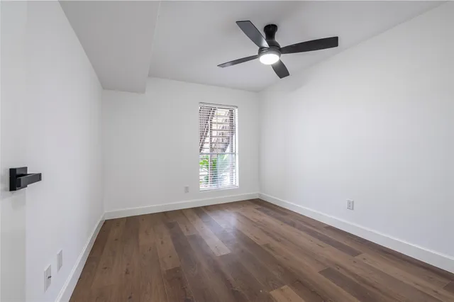 an empty room with wooden floor a ceiling fan and windows