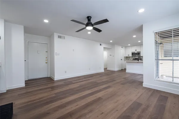 an empty room with wooden floor a ceiling fan and kitchen view