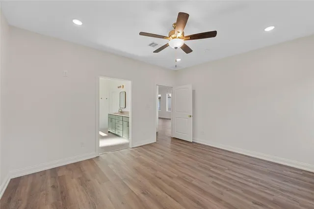 an empty room with wooden floor ceiling fan and windows