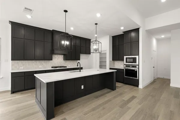 a large kitchen with a large counter top space a sink stainless steel appliances and cabinets